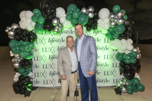 Two men in suits stand smiling before a decorative backdrop of green, white, silver, and black balloons featuring "LUXE" and "lifestyle" logos at night—celebrating the 2025 Men of Influence among this year's influential people. Lifestyle