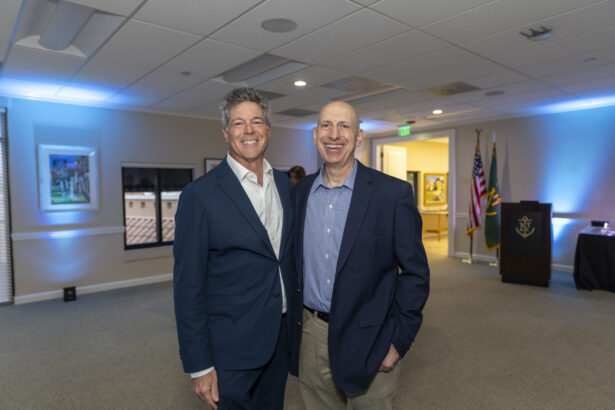 Two men wearing suits stand smiling together in a well-lit room adorned with framed pictures, American flags, and a podium—capturing a moment among the influential people 2025. Lifestyle